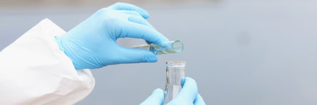 Scientist in gloves and protective suit pours dirty water from test tube into flask