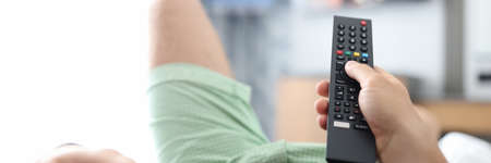 Man lies on bed and switches buttons on TV remote controlの写真素材