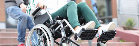 Man lifts wheelchair up steps with woman closeupの写真素材