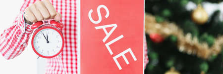 Woman holding red alarm clock and sale plate near new year tree closeupの写真素材