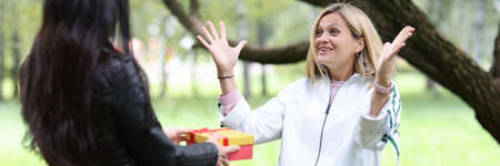 Young woman giving her friend box with gift in parkの写真素材