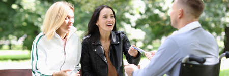 Two young women communicate with a man in wheelchair in park