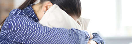 Sad woman sits on couch hiding face in pillow closeupの写真素材