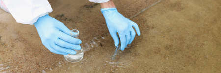 Scientist in protective suit and gloves taking test tube from lake closeup