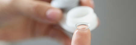 Woman pulling contact lens out of plastic container with her finger closeup