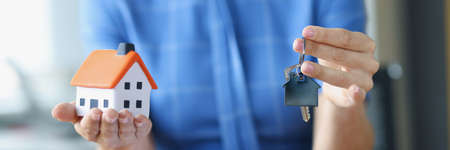 Woman holding toy house and keys over documents closeup