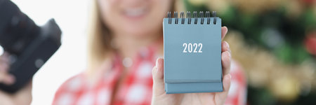Woman photographer in santa hat holding calendar for 2022 near New Year tree closeupの写真素材