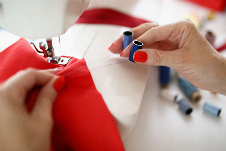Seamstress hands hold blue thread and red cloth