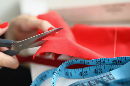 Female hands cut red cloth with scissors