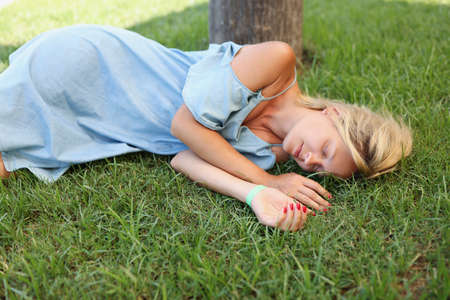 A woman in a blue dress sleeps on the green grass, close-upの写真素材
