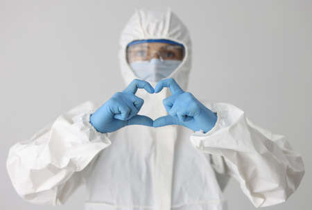 Doctor in protective suit and mask and glasses holds heart gesture