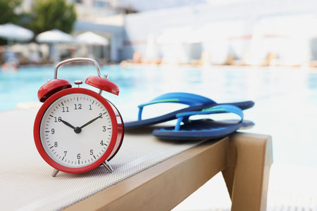 Flip flops alarm clock on deck chair by poolの写真素材