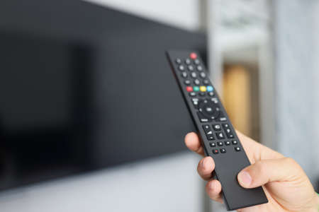 Black remote control in hand in front of TVの写真素材