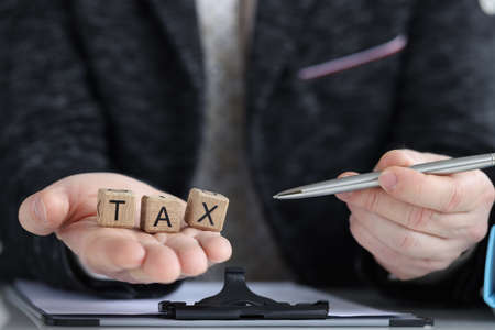 Inscription tax on cubes and businessman holds penの写真素材