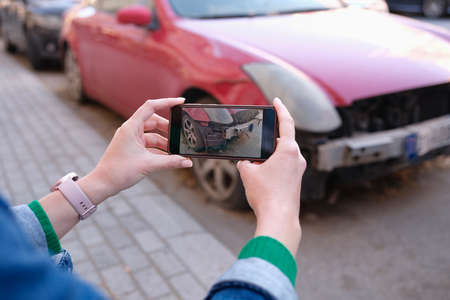 Female hands taking pictures of car damage on mobile phone closeupの写真素材