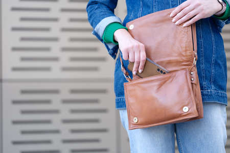 Woman putting mobile phone in brown leather handbag closeupの写真素材