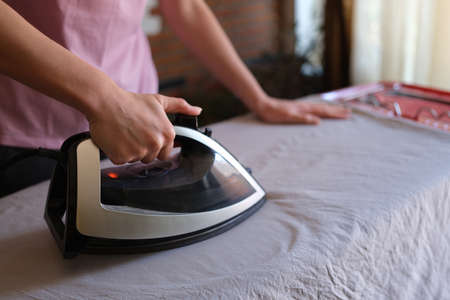 Woman with iron in hands irons clothes on ironing boardの写真素材