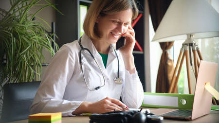 Smiling female doctor talking on phone at workplace in clinicの写真素材