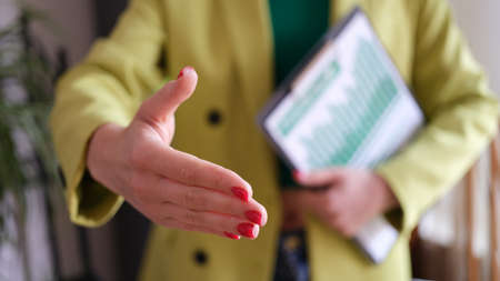 Business partner extends hand for handshake and holds financial chartsの写真素材
