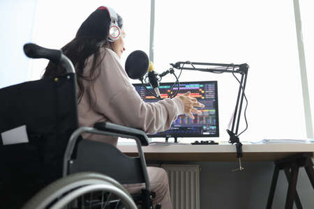 Woman in wheelchair speaks into microphone in front of computerの写真素材