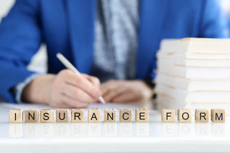 Man filling insurance claim form, word collected of wooden cubesの写真素材