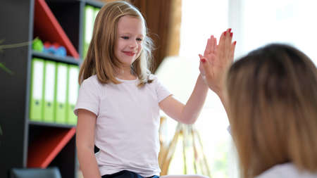 Happy little preschool girl giving high five to doctor at meeting in hospital