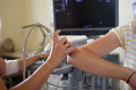 Doctor conducts ultrasound examination of elbow joint in clinic closeup
