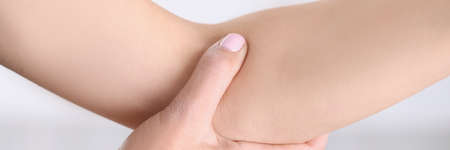A woman presses the fold of her arm, on a gray background