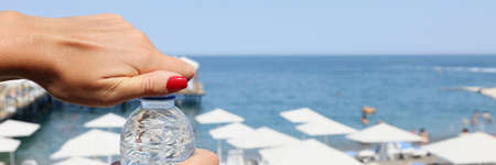 Female hands open a bottle of water on a beach, blurryの写真素材