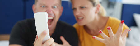 Couple yelling into phone while sitting on the bed in the hotelの写真素材