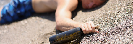 A drunk man with a bottle lies on the wet sand, blurryの写真素材