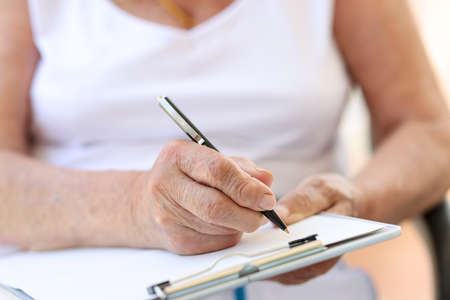 Old woman hands filling form in clinic or in hospice