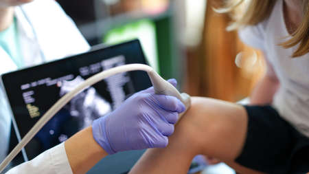 Specialist making ultrasound diagnostics of knee joint of little child