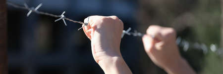 Woman holding hands on barbed wire closeupの写真素材