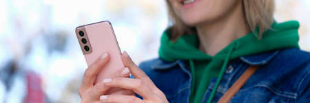 Young woman holding pink mobile phone in park and smiling closeupの写真素材