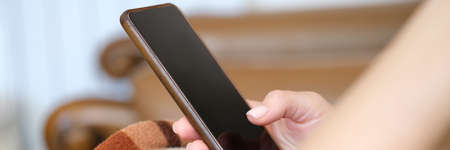 Woman under plaid chatting in social networks using mobile phone closeup