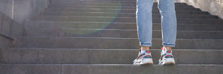 Tired woman in sneakers standing in front of long staircase with stepsの写真素材