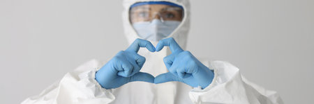 Doctor in protective suit and mask and glasses holds heart gesture