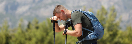 Tired man with Scandinavian walking sticks on mountain