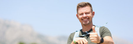 Smiling man holding thumbs up holds Scandinavian sticks and stands on mountain