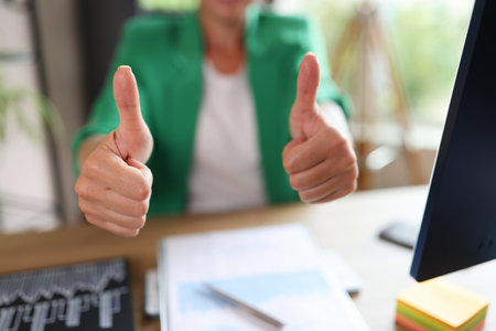 Business woman with thumbs up in office and table with computer and financial documents.の写真素材