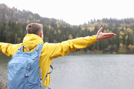 Young casual traveler with backpack looks into the distance at lake and mountains.の写真素材