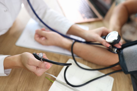Close up of doctor using sphygmomanometer with stethoscope checks blood pressure of patient in hospital.の写真素材