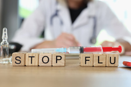 Stop flu words on wooden cubes and vaccine syringe on table, doctor in background.の写真素材
