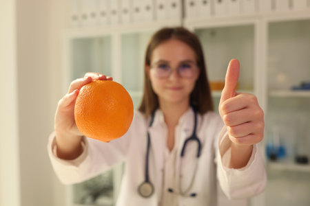 Doctor nutritionist holding orange in his hands and showing thumbs up closeupの写真素材