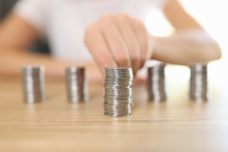 Womans hand lays out piles of coins on wooden table.