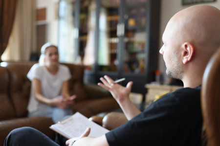 Psychologist is talking to patient while sitting on chair in office during psychotherapy session.の写真素材