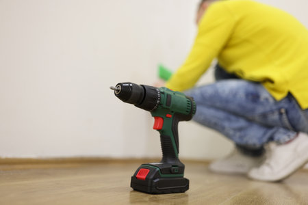 Close-up of drill standing on floor, professional handyman in background.