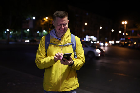Man holds his smartphone and looks at screen of phone while standing on road.の写真素材