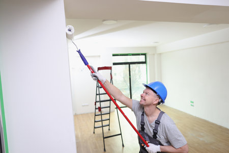 Happy decorator paints house wall with roller brush and white paint.の写真素材